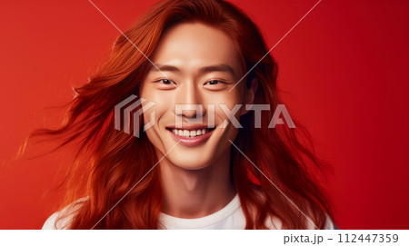 Handsome young male guy smile Asian with long red hair, on red background, banner, copy space, portrait. 112447359