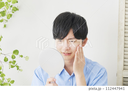 鏡を見て肌トラブルに悩む若い男性 112447941