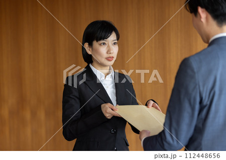 社外秘の封筒を渡すビジネスウーマン 112448656