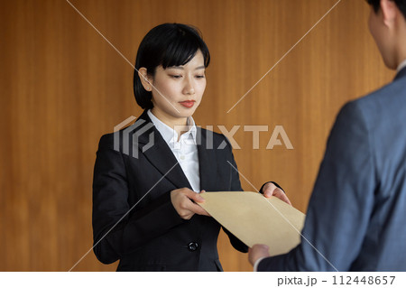 社外秘の封筒を渡すビジネスウーマン 112448657