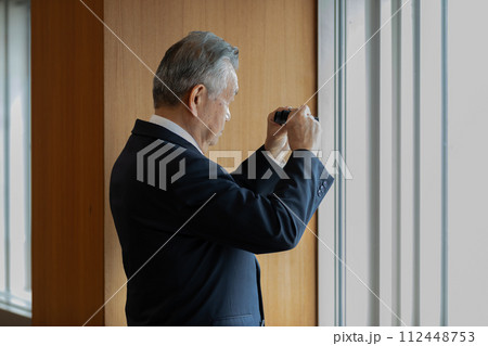 双眼鏡で眼下のビルを覗くシニアビジネスマン 112448753