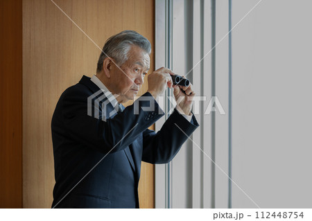 双眼鏡で眼下のビルを覗くシニアビジネスマン 112448754