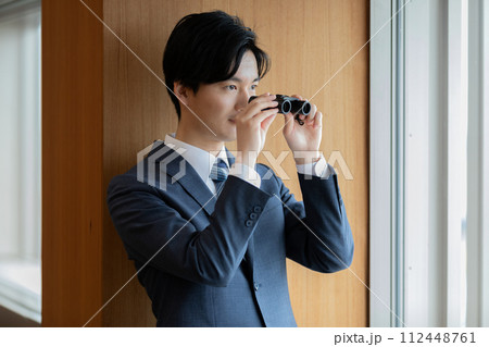 双眼鏡で眼下のビルを覗くビジネスマン 112448761
