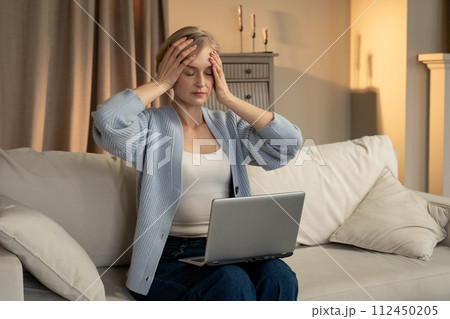 Frustrated Woman Sitting on Sofa With Laptop Covering Her Face With Hand Frustrated Woman Sitting on Sofa With Laptop Covering Her Face With Hand 112450205
