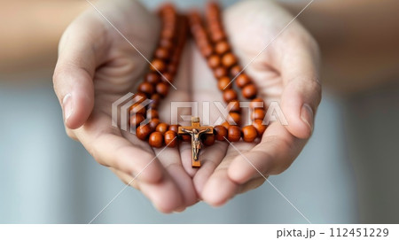 Soulful prayer: a man in quiet devotion, hands clasped around a rosary cross, seeking solace and spiritual connection, capturing the essence of serene contemplation, faith, and religious devotion. 112451229