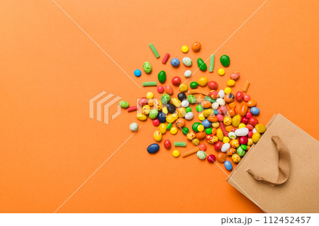 shopping paper gift bag in corner full of assorted traditional candies falling out on colored background with copy space. Happy Holidays sale concept shopping paper gift bag in corner full of assorted traditional candies falling out on colored background with copy space. Happy Holidays sale concept 112452457