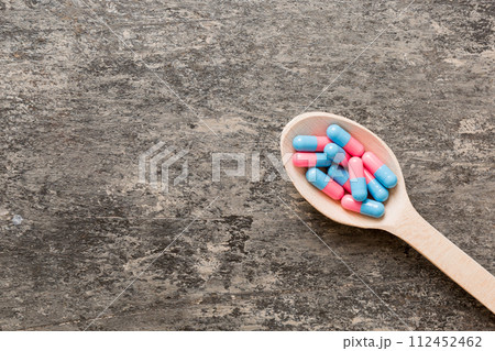 Vitamin capsules in a spoon on a colored background. Pills served as a healthy meal. Red soft gel vitamin supplement capsules on spoon 112452462