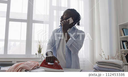 Distracted man talking on phone not paying attention to hot iron on clothes Distracted man talking on phone not paying attention to hot iron on clothes 112453386