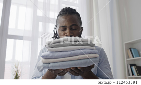 African American man enjoying the smell of freshly washed and ironed clothes, new fabric softener African American man enjoying the smell of freshly washed and ironed clothes, new fabric softener 112453391