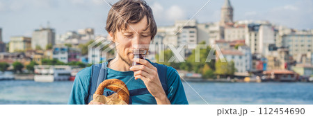 BANNER, LONG FORMAT Man in Istanbul having breakfast with Simit and a glass of Turkish tea. Glass of Turkish tea and bagel Simit against golden horn bay and the Galata Tower in Istanbul, Turkey 112454690