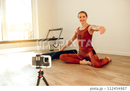 Woman yoga instructor recording online training with smartphone and tripod in fitness studio Woman yoga instructor recording online training with smartphone and tripod in fitness studio 112454987