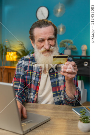 Happy senior man using bank credit card and laptop for online shopping payments at home office 112455005