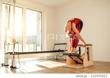 Woman in sports wear having workout on reformer machine in yoga studio Woman in sports wear having workout on reformer machine in yoga studio 112455021