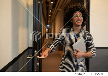 Man in striped shirt with laptop in hands opening door in the hotel 112455918