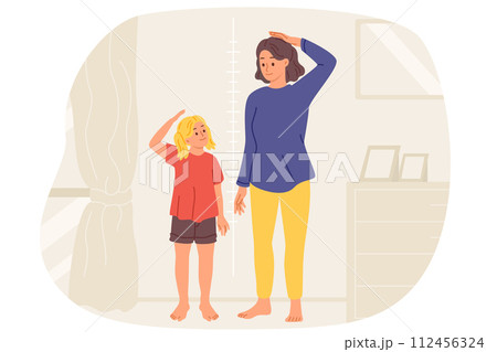 Little girl and mother measure own height standing near wall with marks in apartment. 112456324
