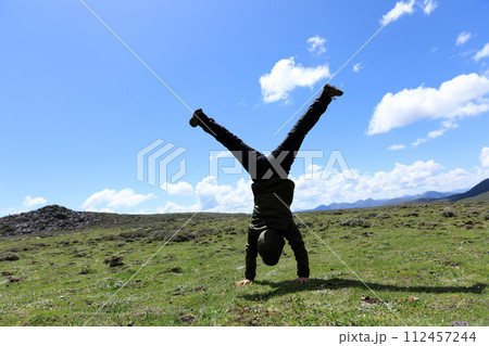 Woman hiker doing a handstand on high altitude mountain meadow 112457244