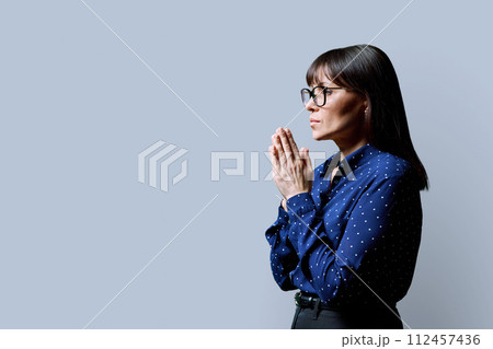 Serious mature woman folded her hands in prayer, meditation on gray background Serious mature woman folded her hands in prayer, meditation on gray background 112457436