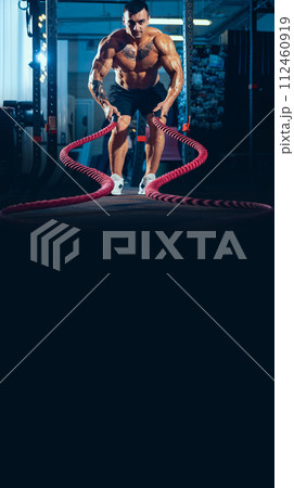 Young healthy man, athlete doing exercise with the ropes in the gym. Male model training hard his upper body Young healthy man, athlete doing exercise with the ropes in the gym. Male model training hard his upper body 112460919