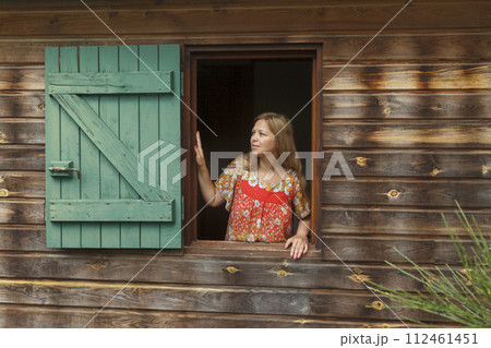Woman in window of wooden house Woman in window of wooden house 112461451