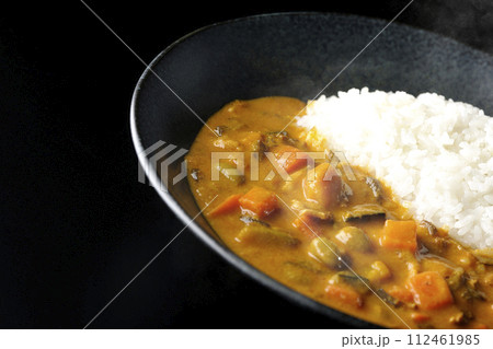 豚肉、かぼちゃ、人参などの野菜が沢山入った熱々カレーライスを黒背景で撮影 112461985