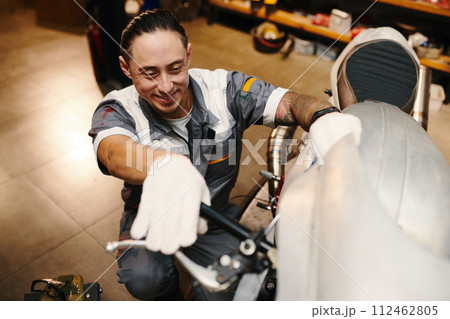 Smiling repairman checking leverage of motorcycle 112462805