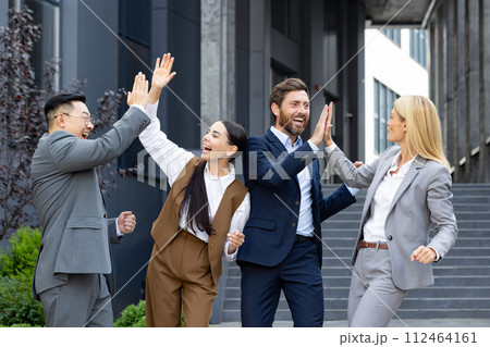 A young interracial business team is happy about a successful deal and partnership. A group of men and women stand outside an office center and high five each other, congratulating on victory. A young interracial business team is happy about a successful deal and partnership. A group of men and women stand outside an office center and high five each other, congratulating on victory. 112464161