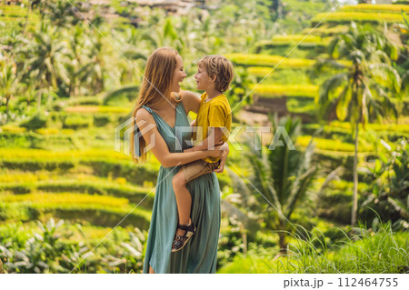 Mom and son on the rice field in the background of rice terraces, Ubud, Bali, Indonesia. Traveling with children concept. Teaching children in practice Mom and son on the rice field in the background of rice terraces, Ubud, Bali, Indonesia. Traveling with children concept. Teaching children in practice 112464755