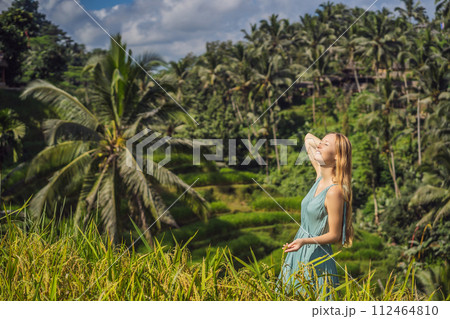 Beautiful young woman walk at typical Asian hillside with rice farming, mountain shape green cascade rice field terraces paddies. Ubud, Bali, Indonesia. Bali travel concept 112464810