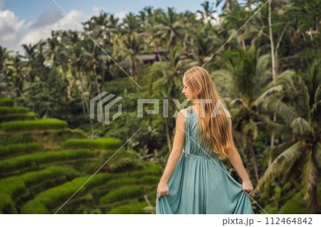 Beautiful young woman walk at typical Asian hillside with rice farming, mountain shape green cascade rice field terraces paddies. Ubud, Bali, Indonesia. Bali travel concept 112464842