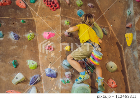 little boy climbing a rock wall in special boots. indoor little boy climbing a rock wall in special boots. indoor 112465813