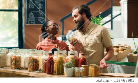 Seller helping people with information about homegrown products and sustainable lifestyle, presenting organic natural vegetables. Couple looking for vegan food alternatives at local eco store. 112465903