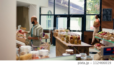 Customer looking at fresh veggies on shelves at local zero waste eco store, choosing to buy homegrown produce for sustainable lifestyle and vegan nutrition. Man doing shopping at ecological shop. Customer looking at fresh veggies on shelves at local zero waste eco store, choosing to buy homegrown produce for sustainable lifestyle and vegan nutrition. Man doing shopping at ecological shop. 112466019