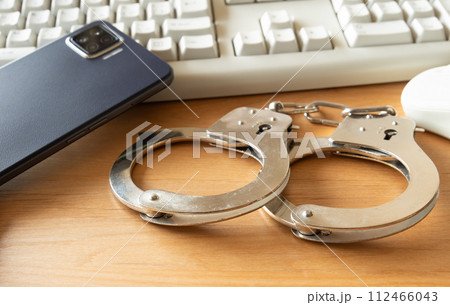 手錠とインターネット　犯罪イメージ　サイバー犯罪　違法行為　不正利用　スマホ　パソコン 112466043