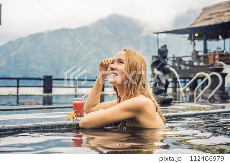 Geothermal spa. Woman relaxing in hot spring pool against the lake. hot springs concept. Drinking guava juice Geothermal spa. Woman relaxing in hot spring pool against the lake. hot springs concept. Drinking guava juice 112466979
