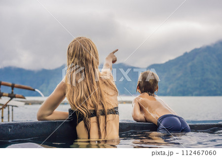 Mom and son travelers in Hot Springs in Bali on the background of lake. Traveling with children concept Mom and son travelers in Hot Springs in Bali on the background of lake. Traveling with children concept 112467060
