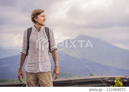 Outdoor portrait of Young man looking on Batur volcano and Agung mountain view at morning from Kintamani, Bali, Indonesia 112468072