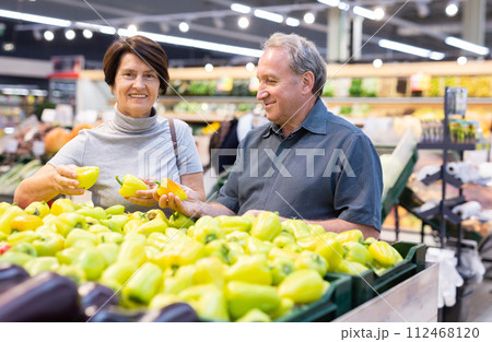 Smiling happy couple is choosing bell peppers and other vegetables in supermarket 112468120