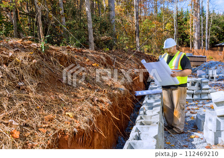 In mounting retaining wall by cement blocks, construction workers study blueprint plan In mounting retaining wall by cement blocks, construction workers study blueprint plan 112469210