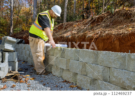 Worker studied blueprint plans when mounting retaining walls using cement blocks 112469237