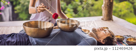 BANNER, LONG FORMAT Nepal Buddha copper singing bowl at spa salon. Young beautiful man doing massage therapy singing bowls in the Spa against a waterfall. Sound therapy, recreation, meditation BANNER, LONG FORMAT Nepal Buddha copper singing bowl at spa salon. Young beautiful man doing massage therapy singing bowls in the Spa against a waterfall. Sound therapy, recreation, meditation 112469426