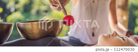 BANNER, LONG FORMAT Nepal Buddha copper singing bowl at spa salon. Young beautiful woman doing massage therapy singing bowls in the Spa against a waterfall. Sound therapy, recreation, meditation 112470030