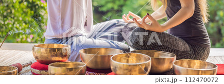BANNER, LONG FORMAT Nepal Buddha copper singing bowl at spa salon. Young beautiful woman doing massage therapy singing bowls in the Spa against a waterfall. Sound therapy, recreation, meditation 112470072