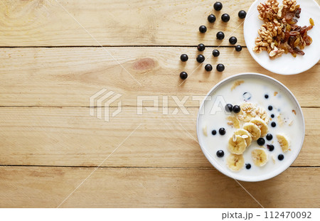 Oatmeal porridgewith bananas, nuts, raisins, blueberries and milk on table on wooden background. Healthy breakfast and diet food. Oatmeal porridgewith bananas, nuts, raisins, blueberries and milk on table on wooden background. Healthy breakfast and diet food. 112470092