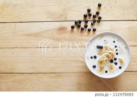 Oatmeal porridgewith bananas, nuts, raisins, blueberries and milk on table on wooden background. Healthy breakfast and diet food. Oatmeal porridgewith bananas, nuts, raisins, blueberries and milk on table on wooden background. Healthy breakfast and diet food. 112470093