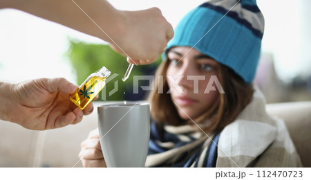 Drops of marijuana oil dripping into cup of sick woman wearing hat closeup Drops of marijuana oil dripping into cup of sick woman wearing hat closeup 112470723