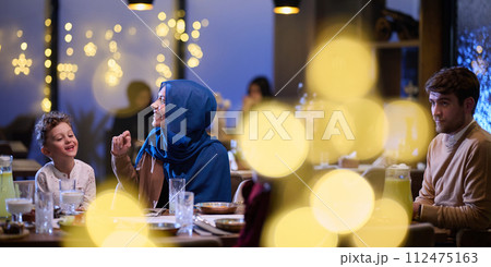 In a modern restaurant, an Islamic couple and their children joyfully await their iftar meal during the holy month of Ramadan, embodying familial harmony and cultural celebration amidst the In a modern restaurant, an Islamic couple and their children joyfully await their iftar meal during the holy month of Ramadan, embodying familial harmony and cultural celebration amidst the 112475163