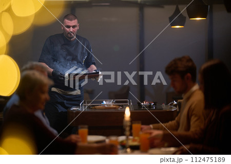 In a restaurant setting, a professional chef presents a sizzling steak cooked over an open flame, while an European Muslim family eagerly awaits their iftar meal during the holy month of Ramadan 112475189