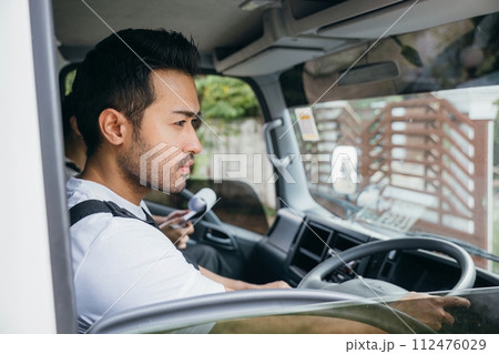 Man driver and mover in a truck for relocation service. Teamwork in transporting and delivering furniture. Smiling employees working confidently. House moving service concept. Man driver and mover in a truck for relocation service. Teamwork in transporting and delivering furniture. Smiling employees working confidently. House moving service concept. 112476029