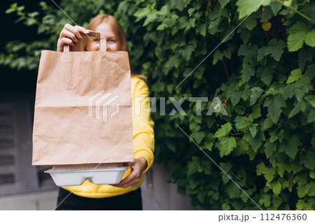 Paper bag and food containers in hands of a smiling woman outdoors. Takeaway food in paper bag Paper bag and food containers in hands of a smiling woman outdoors. Takeaway food in paper bag 112476360