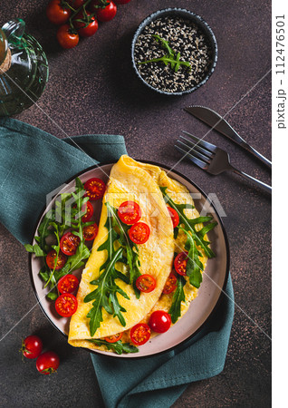 Omelette pancake with cherry tomatoes and arugula on a plate on the table top and  vertical view 112476501